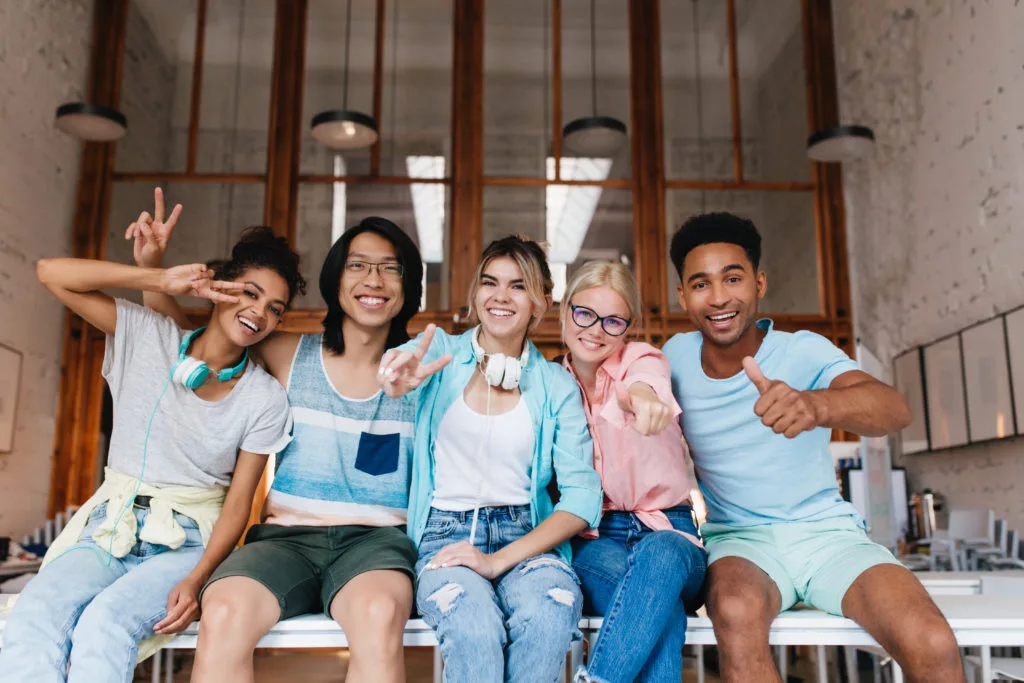 Mädchen aufgeregt blaues Hemd zeigt Zeichen Frieden wertschätzend Gesellschaft Freund guter Tag Innenportrait internationale Studenten glücklich Spaß beim Fotografieren 1024x683 1 jpg Lachen